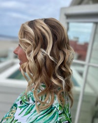 a woman with long wavy blonde hair in front of a palm tree